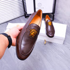 Brown leather slip-on loafer held in hand, gold Medusa emblem