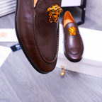 Close-up of brown leather slip-on loafer with gold Medusa emblem