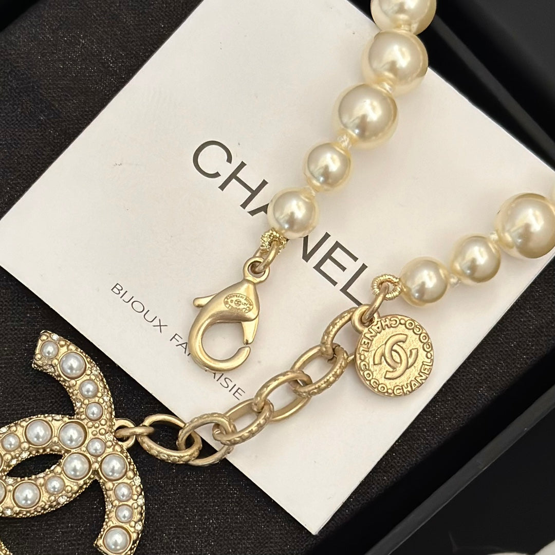 Chanel pearl bracelet with gold-tone chain, logo medallion, and dangling charm