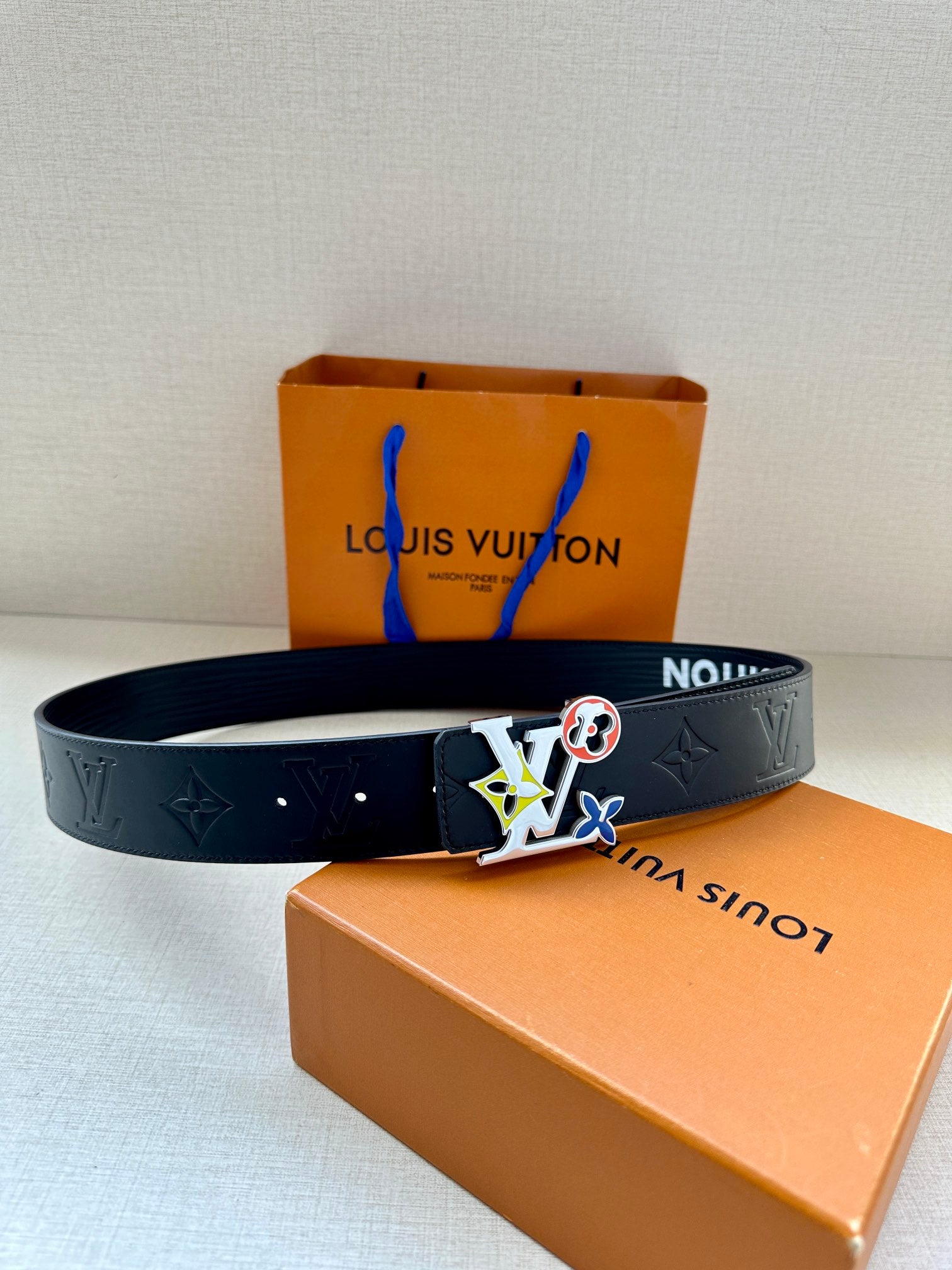 Louis Vuitton belt laid out with multicolor charm buckle on dark navy strap