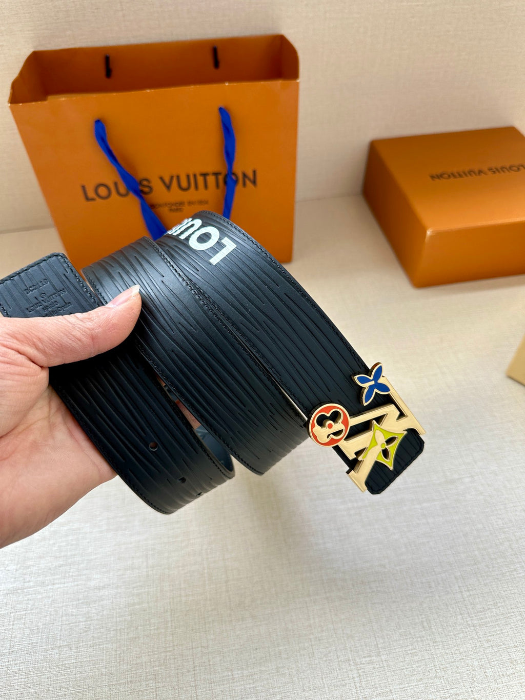 Louis Vuitton belt with textured dark navy strap and multicolor charm buckle, handheld