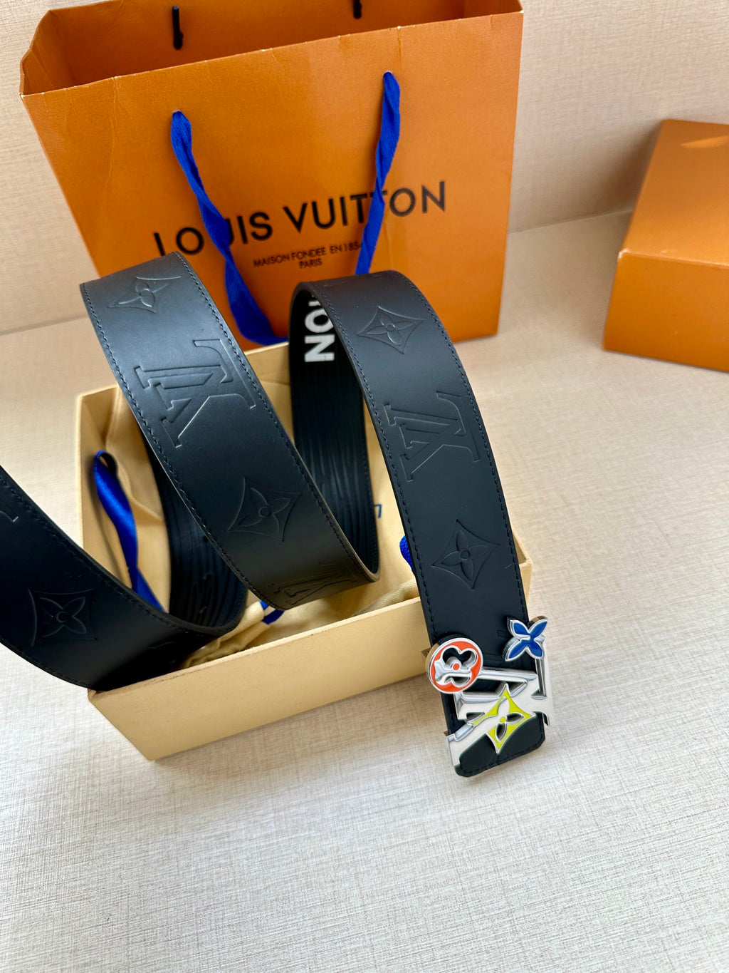 Louis Vuitton belt in box with textured dark navy strap and multicolor charm buckle