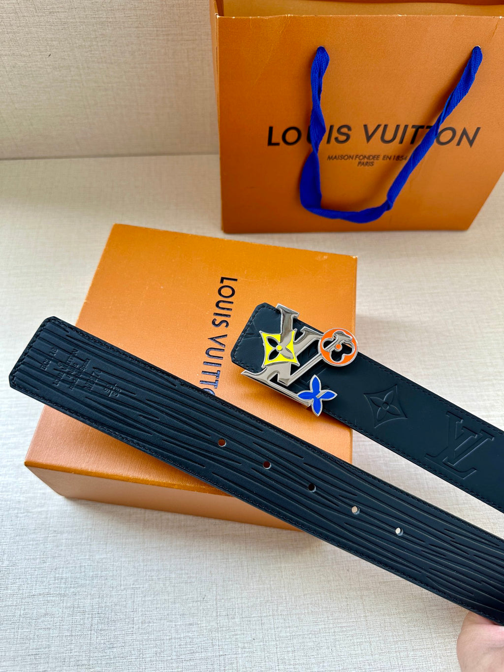 Louis Vuitton belt held out with dark textured navy strap and multicolor square buckle
