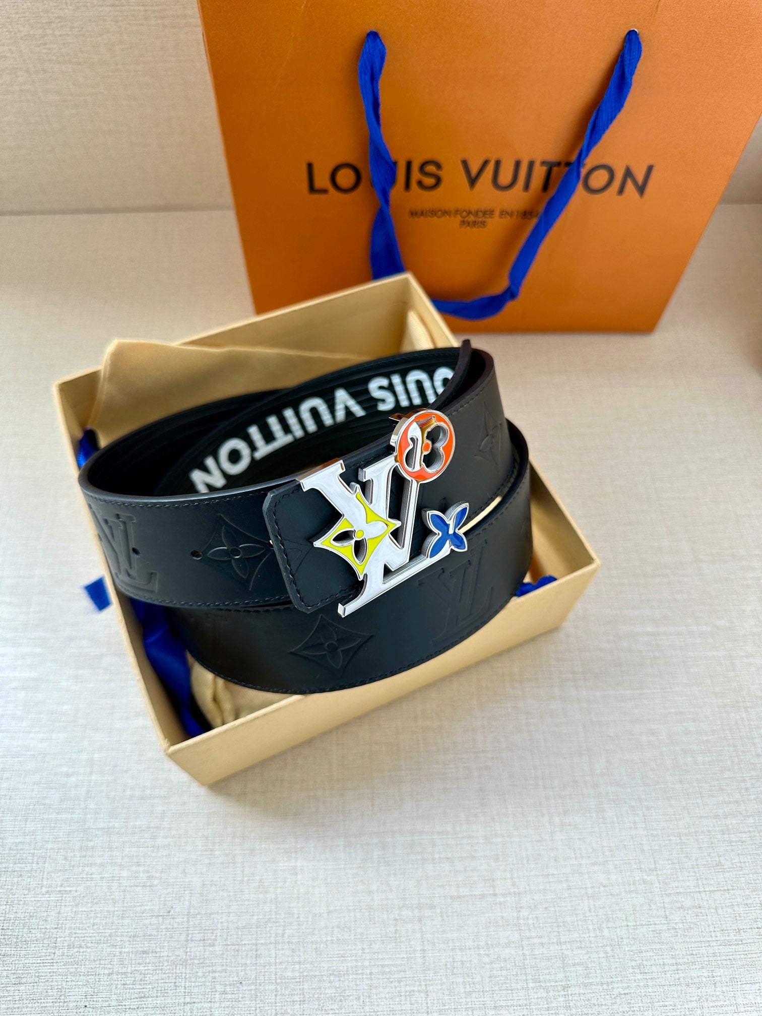 Louis Vuitton belt in open box with dark navy strap and multicolor charm buckle