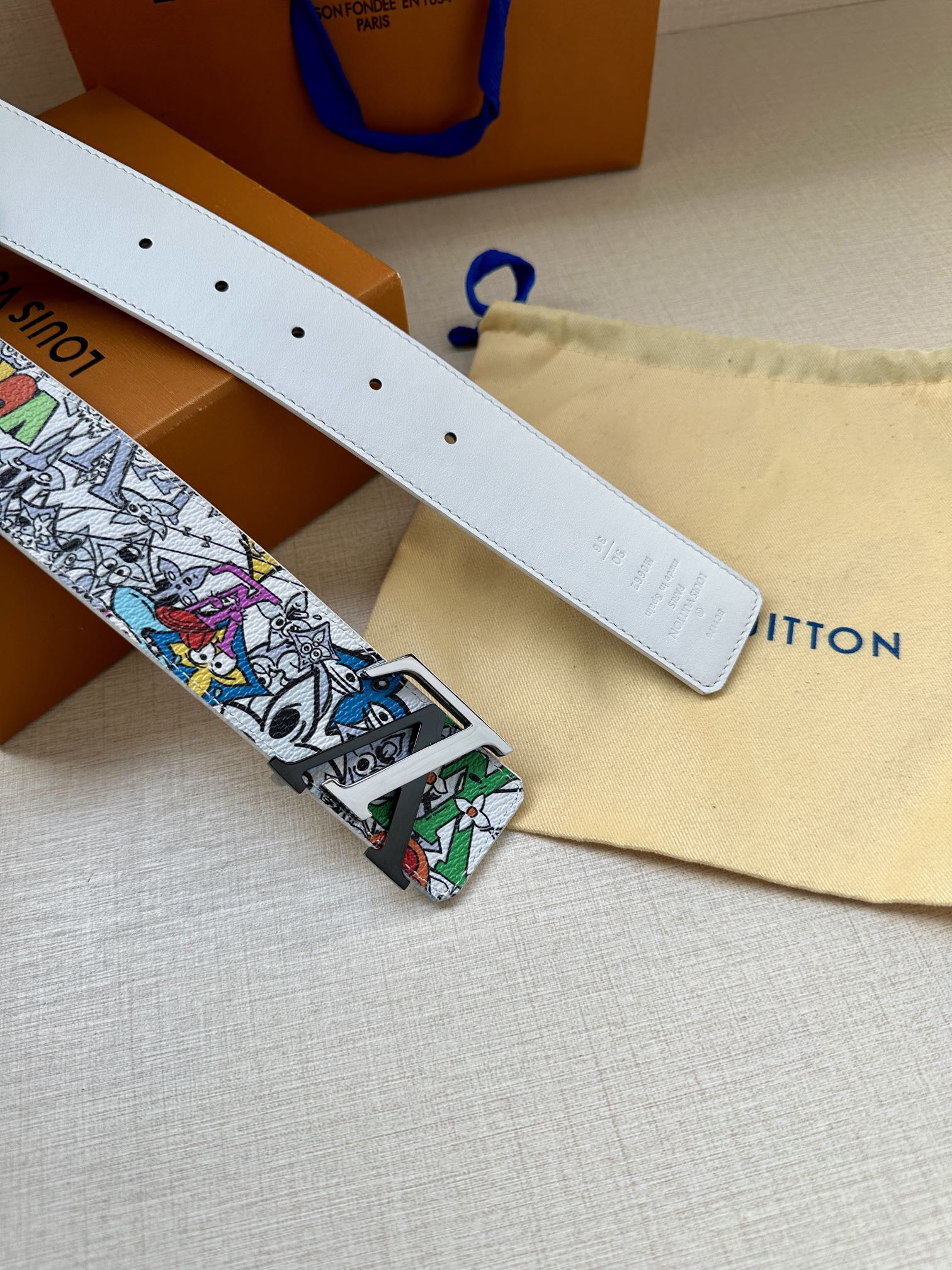 White leather belt with stud holes and multicolor graphic buckle