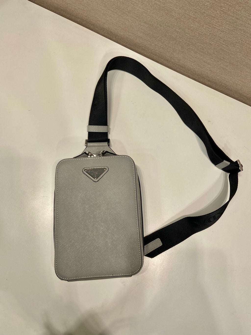Prada mini crossbody bag, light gray with black shoulder strap, overhead view
