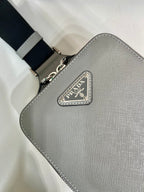 Prada mini bag close-up, light gray textured leather with Prada logo metal patch