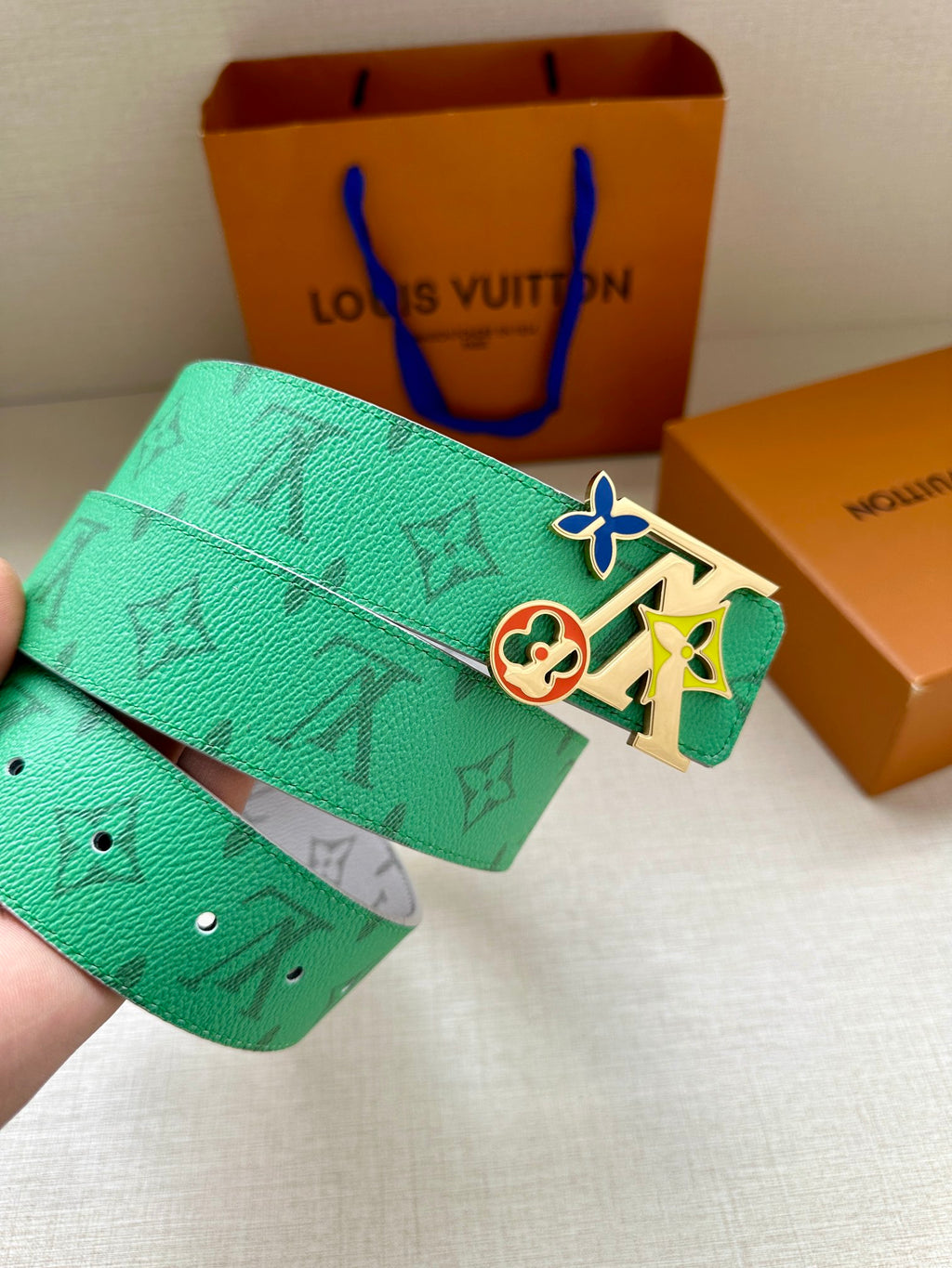 Louis Vuitton belt being held: green monogram strap and silver buckle with colorful charm