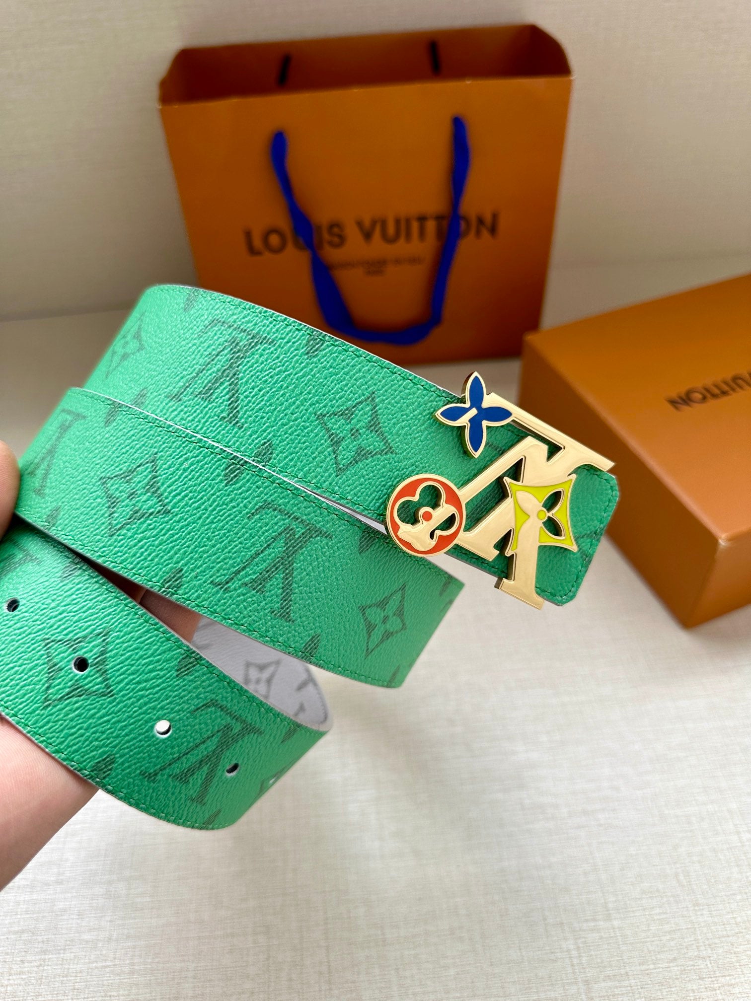 Louis Vuitton belt being held: green monogram strap and silver buckle with colorful charm