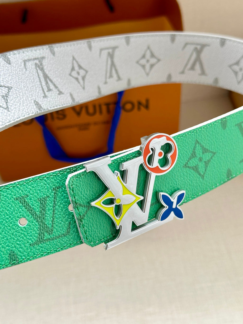 Louis Vuitton belt close-up: green monogram strap and silver buckle with multicolor charm