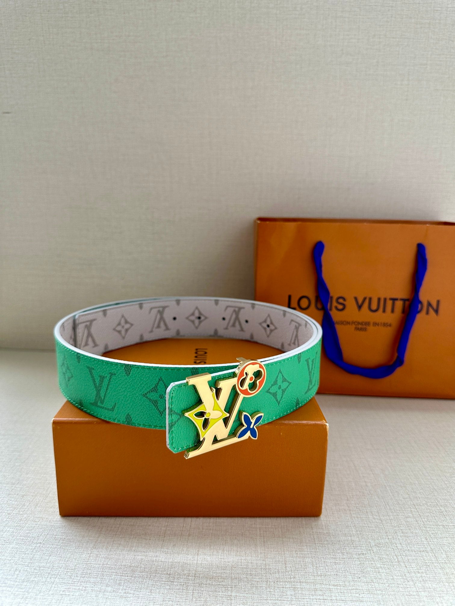 Louis Vuitton belt with green monogram strap and silver buckle, styled on boxes