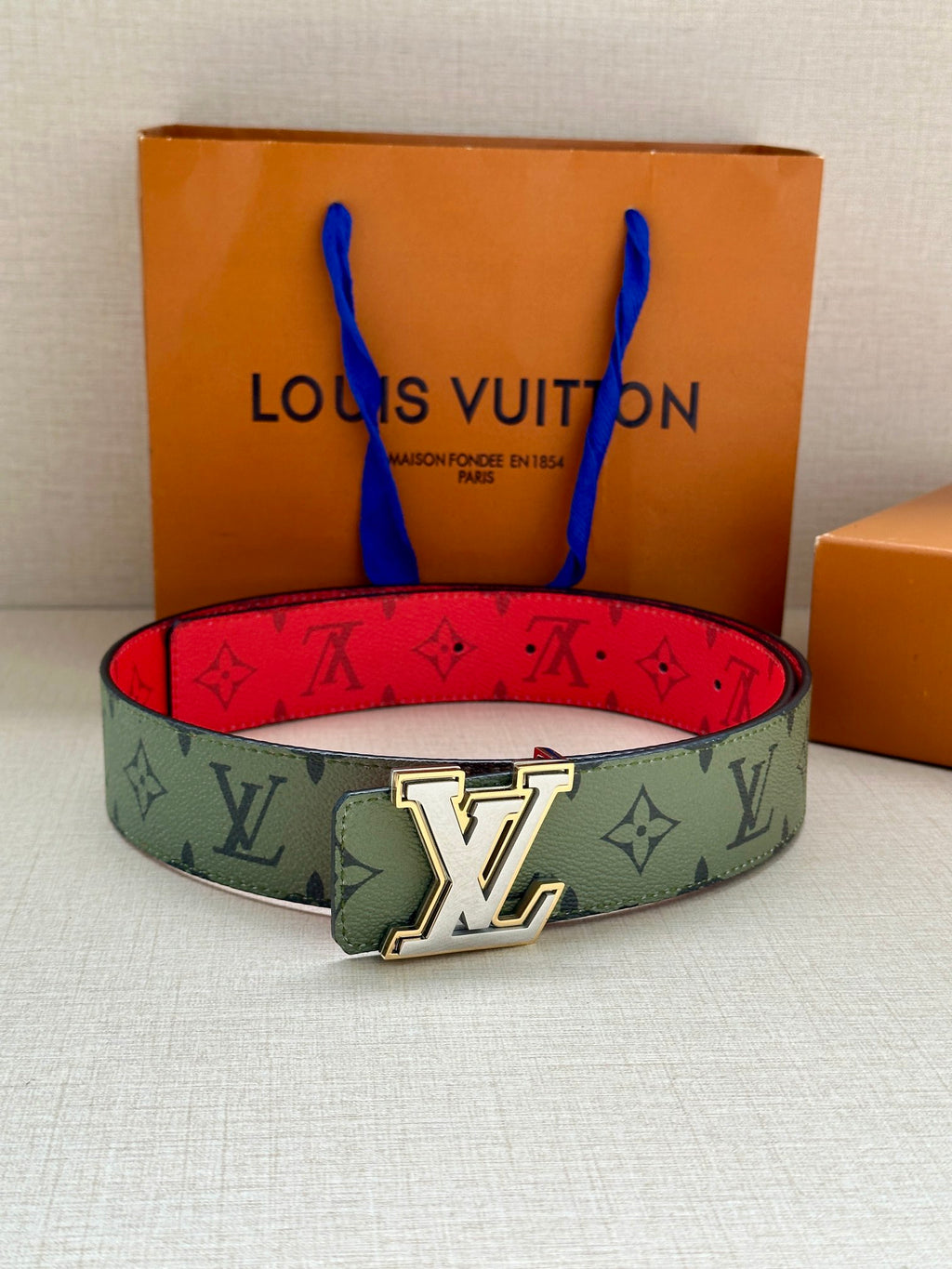 Louis Vuitton belt on display: green monogram strap with red underside and gold-tone LV buckle