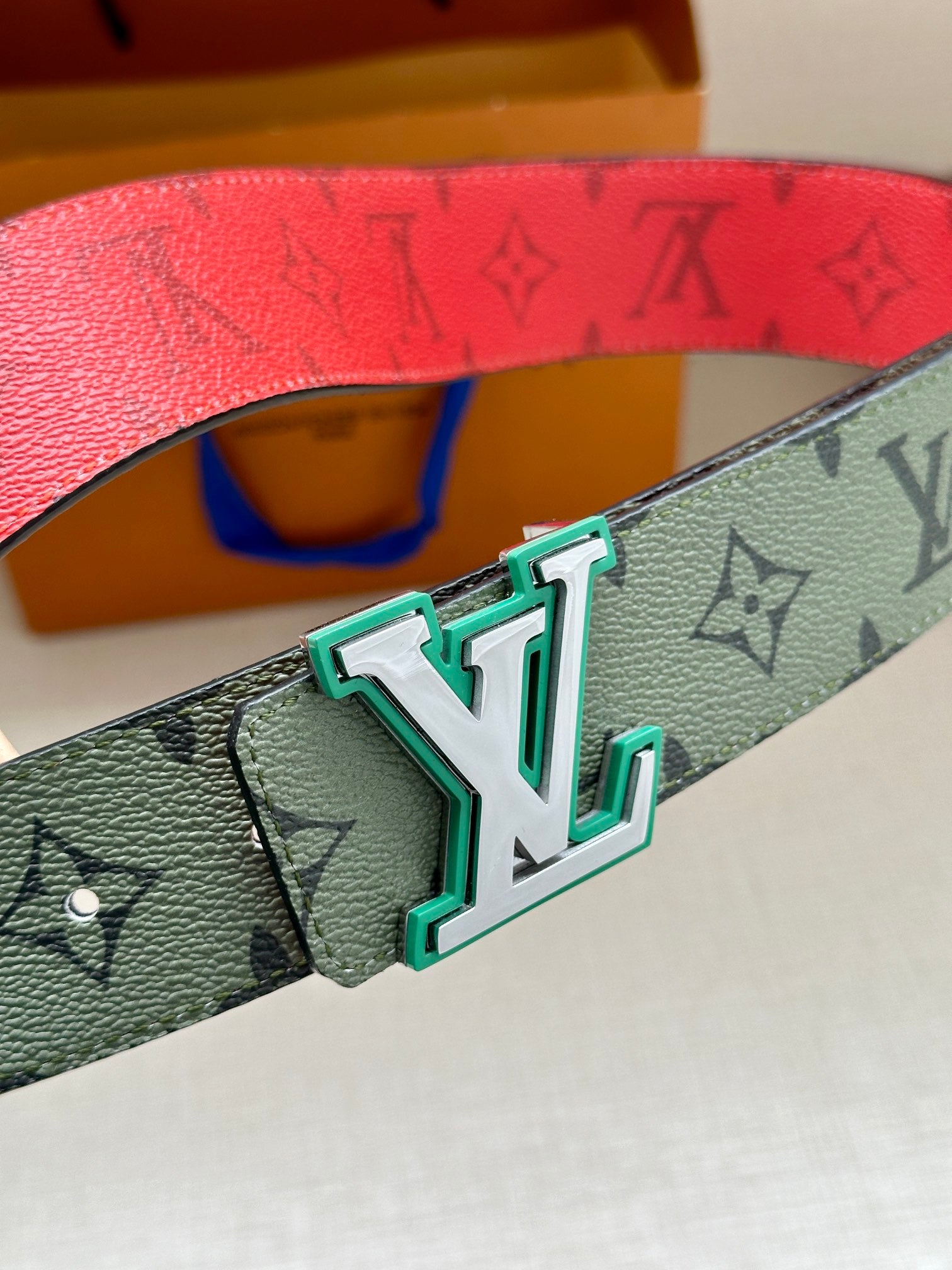 Louis Vuitton belt buckle close-up on green monogram strap with teal frame details