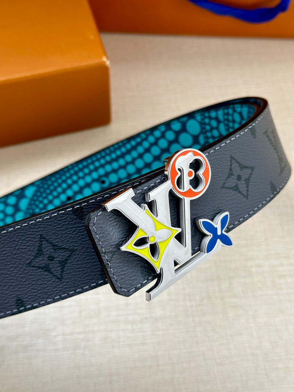 Louis Vuitton belt detail: dark monogram leather with colorful emblem buckle and metal keeper.