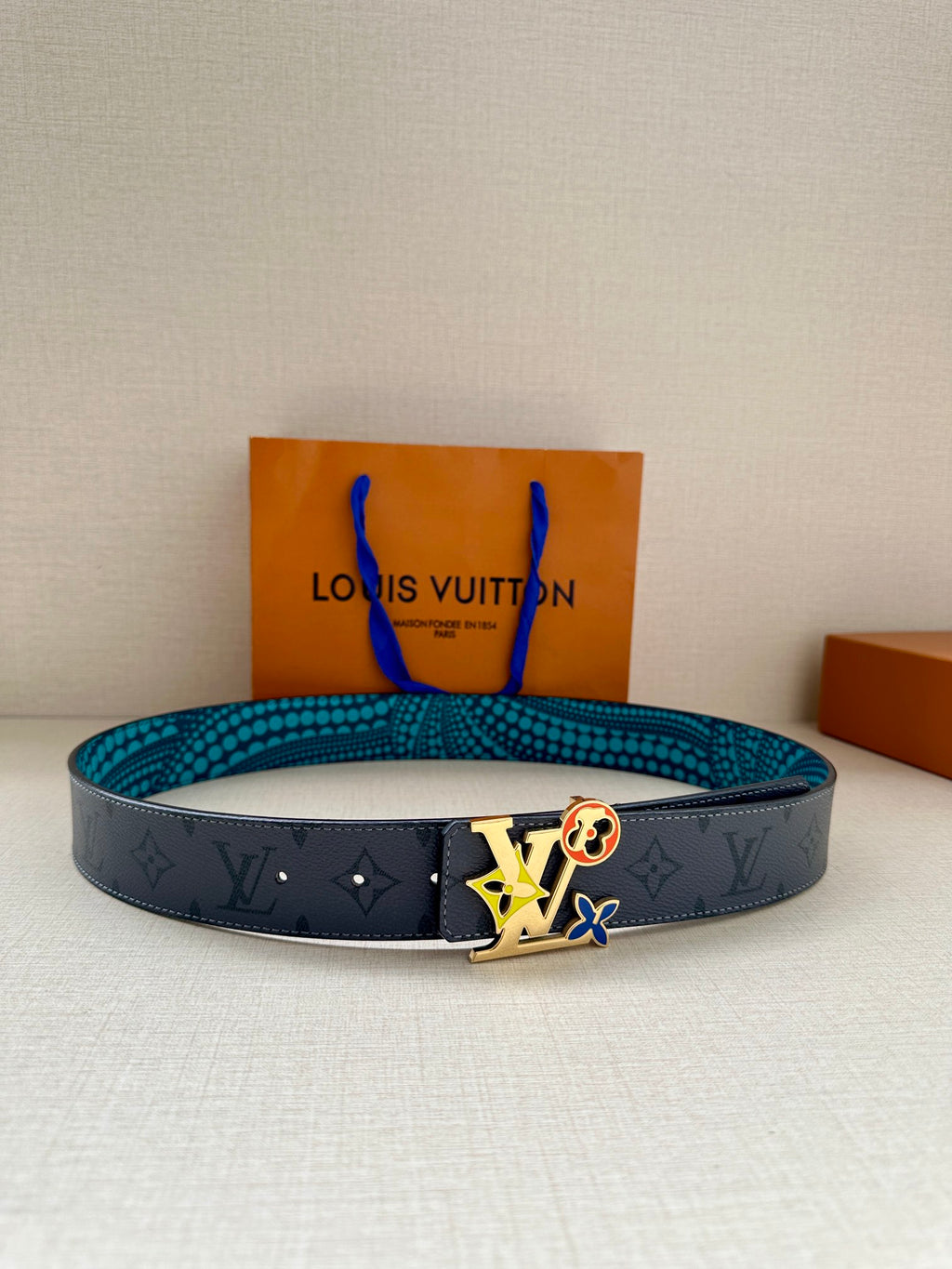 Louis Vuitton belt with dark monogram strap, turquoise dotted lining, and colorful logo buckle.