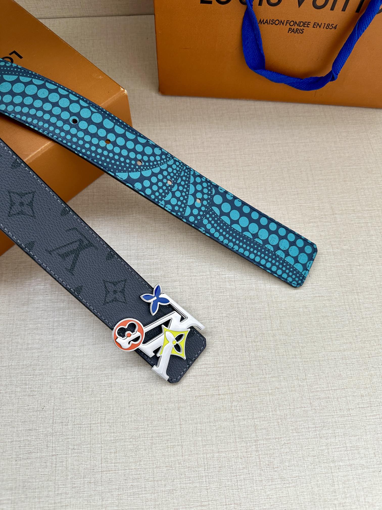 Louis Vuitton belt strap with turquoise dotted underside and dark end with colorful buckle emblem.