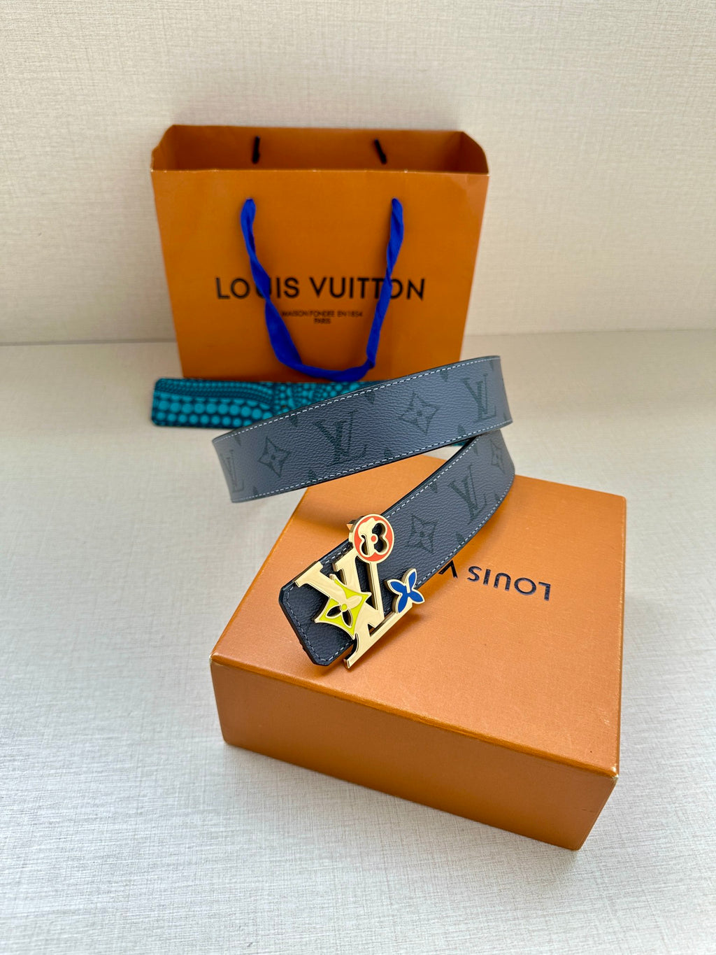 Louis Vuitton belt with dark monogram strap and large colorful logo buckle on box display.