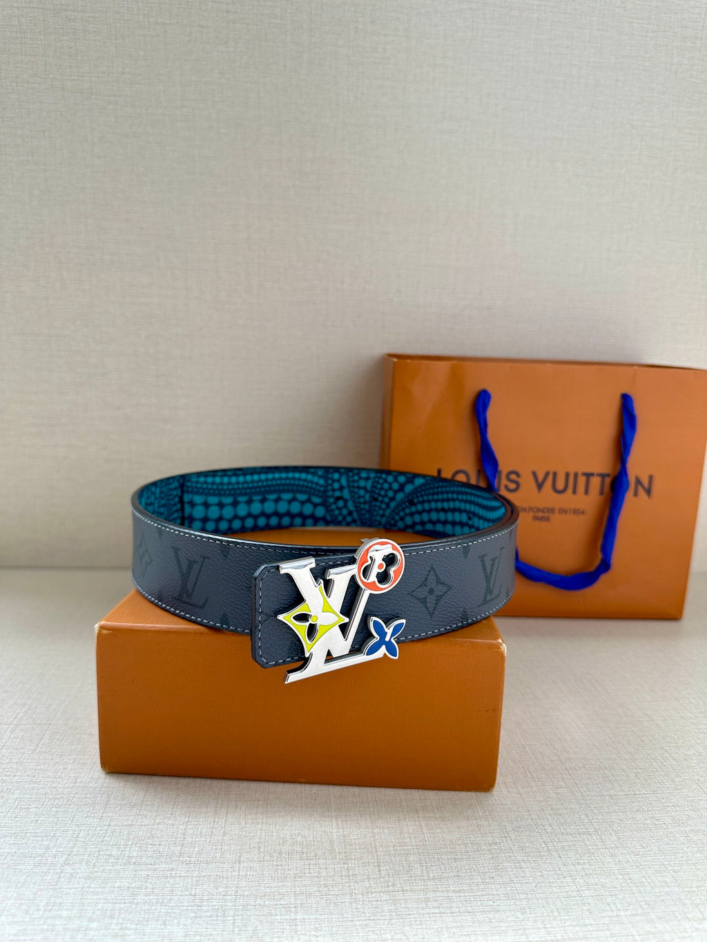 Louis Vuitton belt with dark monogram strap, turquoise dotted lining, and colorful logo buckle.