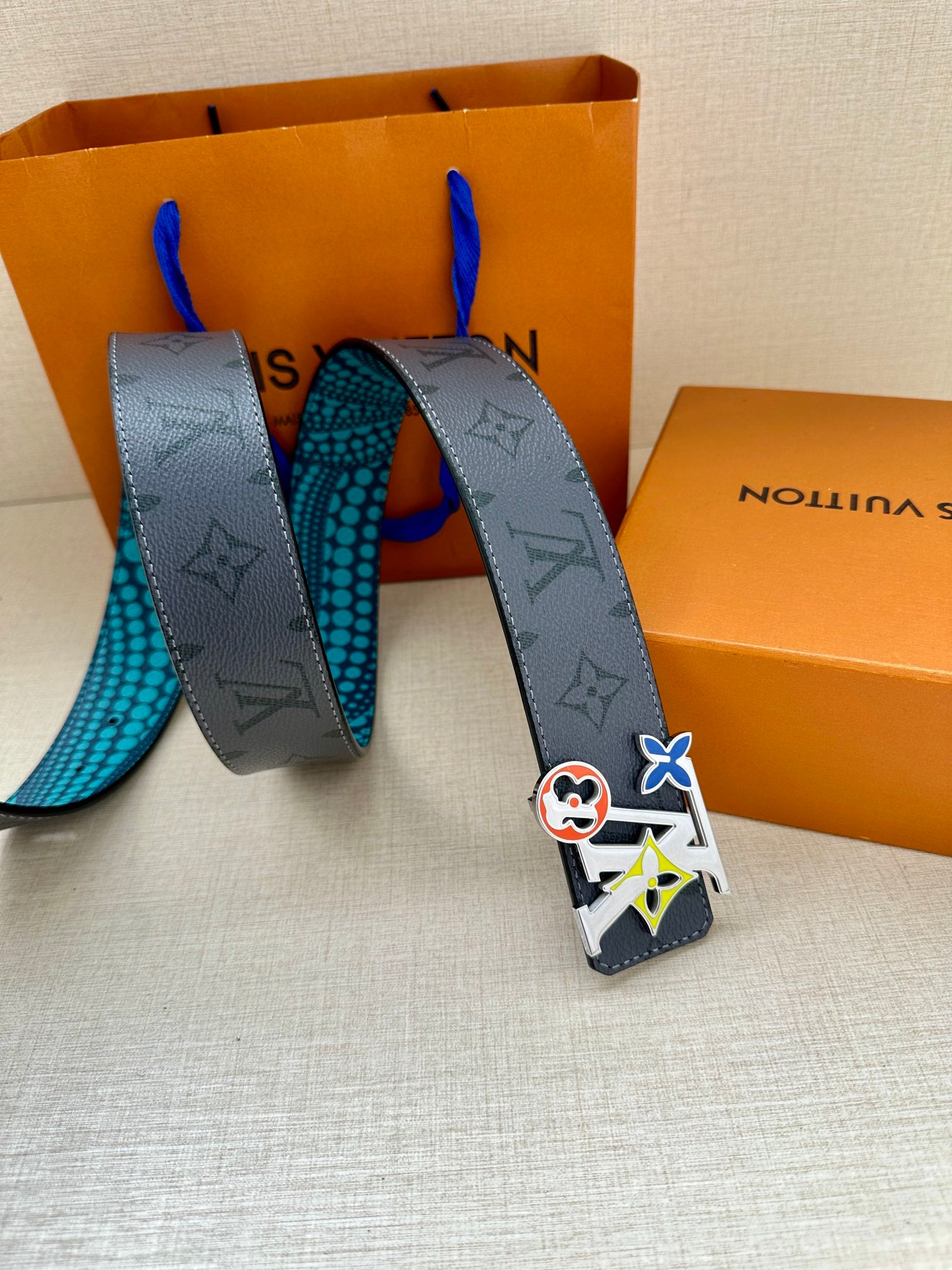 Louis Vuitton belt with dark monogram strap, turquoise dotted underside, and colorful buckle charm.