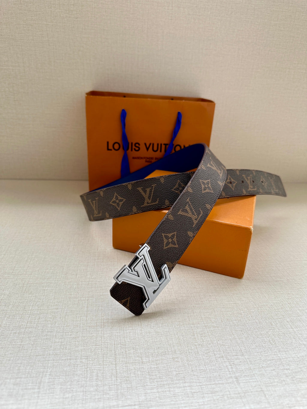 Louis Vuitton monogram belt shown angled, dark canvas with blue leather strap and LV buckle
