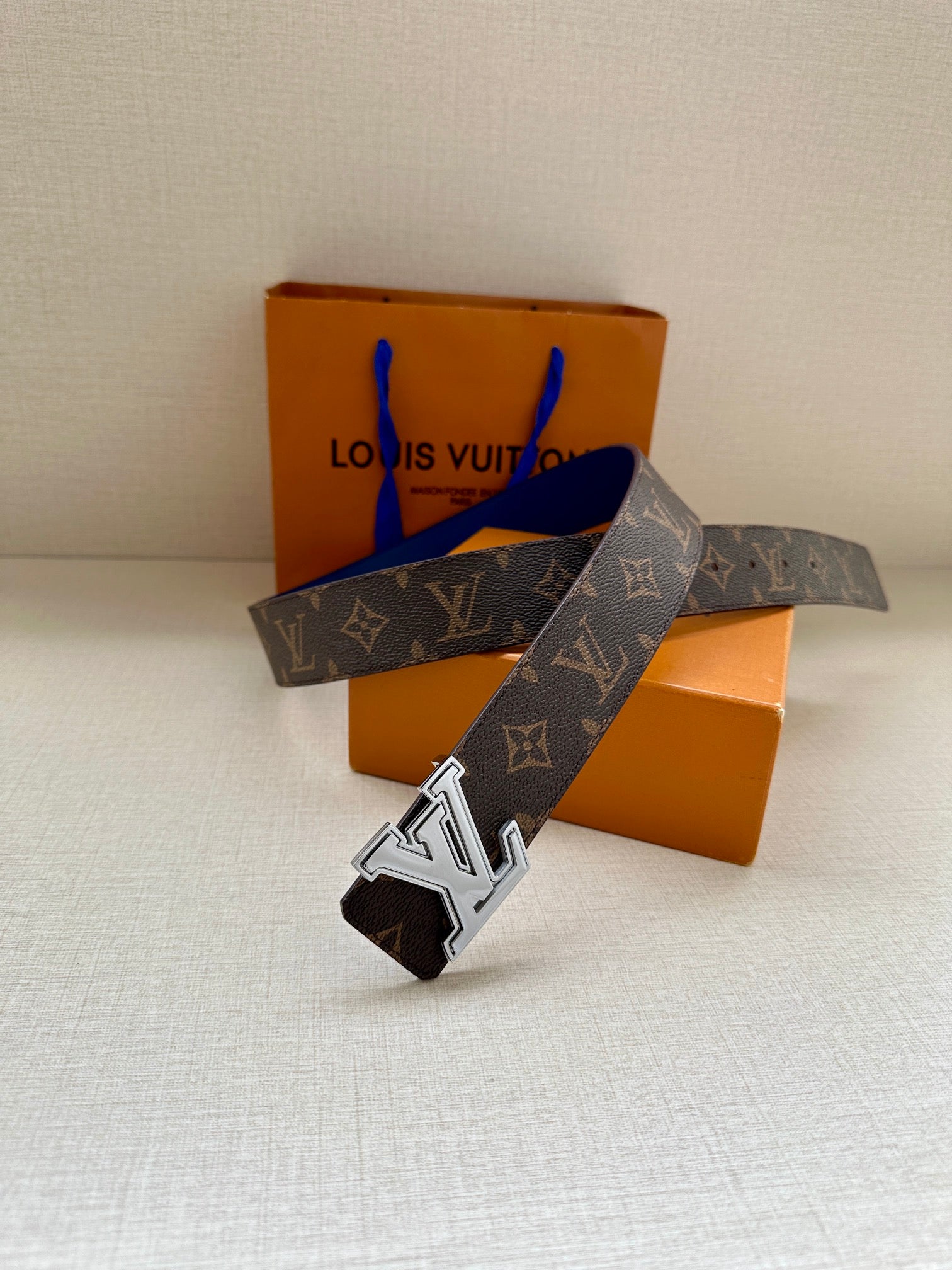 Louis Vuitton monogram belt shown angled, dark canvas with blue leather strap and LV buckle