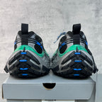 Unisex sneakers rear view on box, black uppers with blue accents and green midsole stripe.