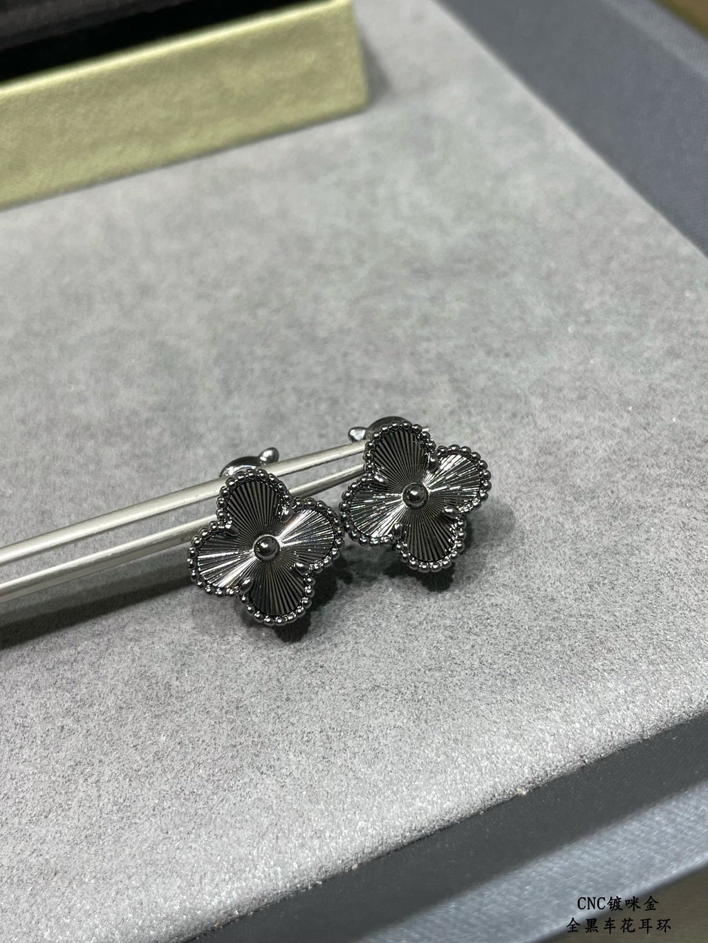 Silver-tone quatrefoil stud earrings on a bar display, close-up