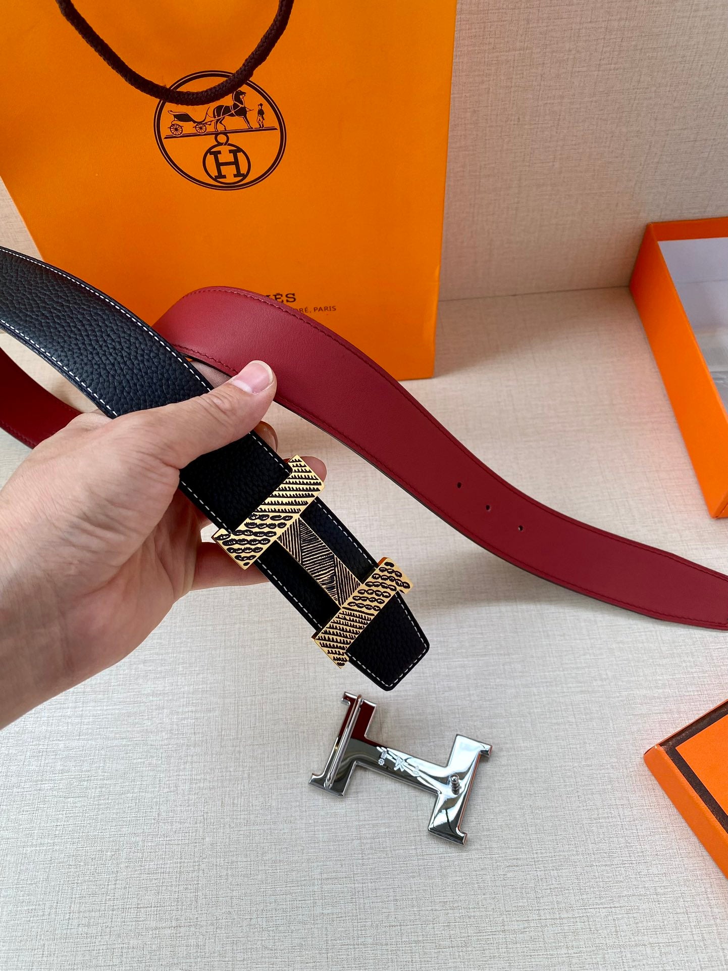 Hermes belt shown with dark blue strap and gold-tone patterned buckle plate
