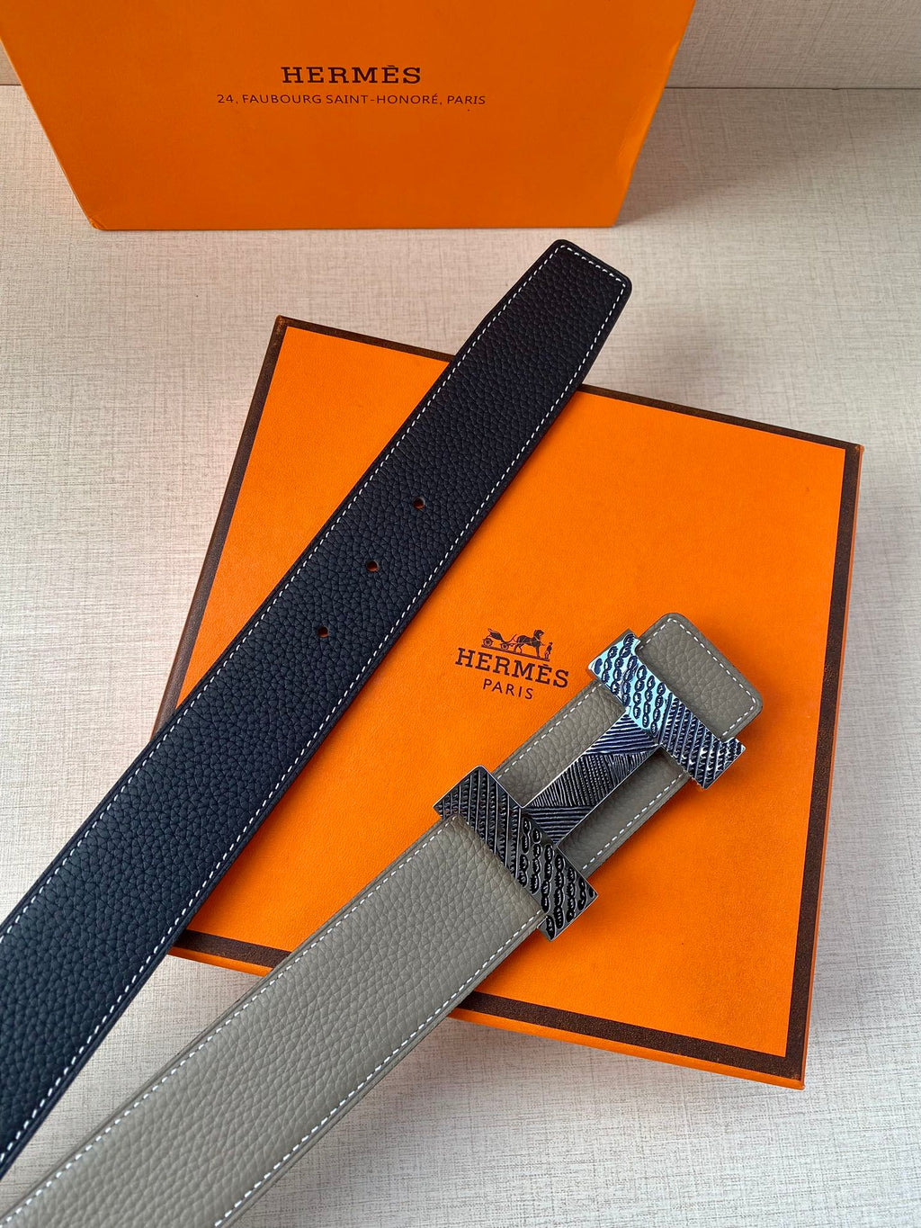Grey leather belt with textured gold-tone clasp and dark lining strip, laid diagonally.