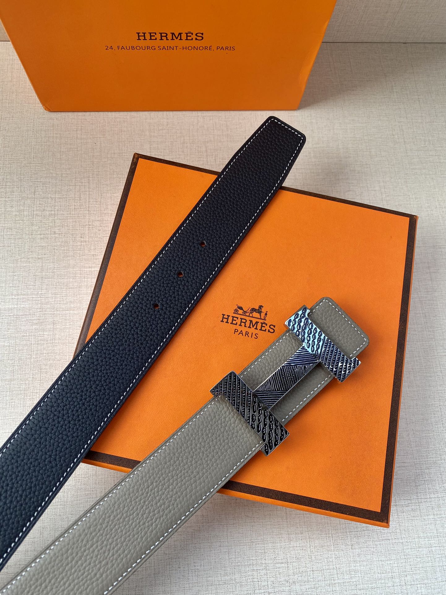 Grey leather belt with textured gold-tone clasp and dark lining strip, laid diagonally.