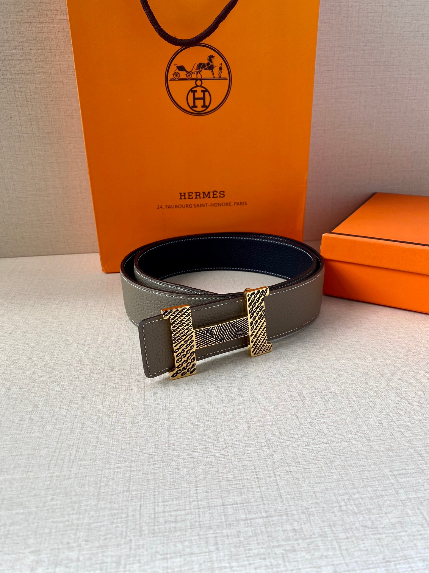 Grey leather belt with dark interior and textured gold-tone buckle, shown flat.
