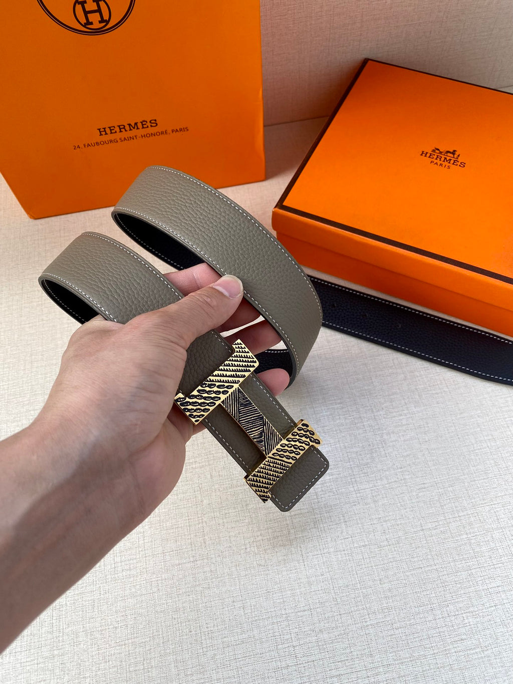 Grey leather belt strap with textured gold-tone buckle, close-up held in hand.
