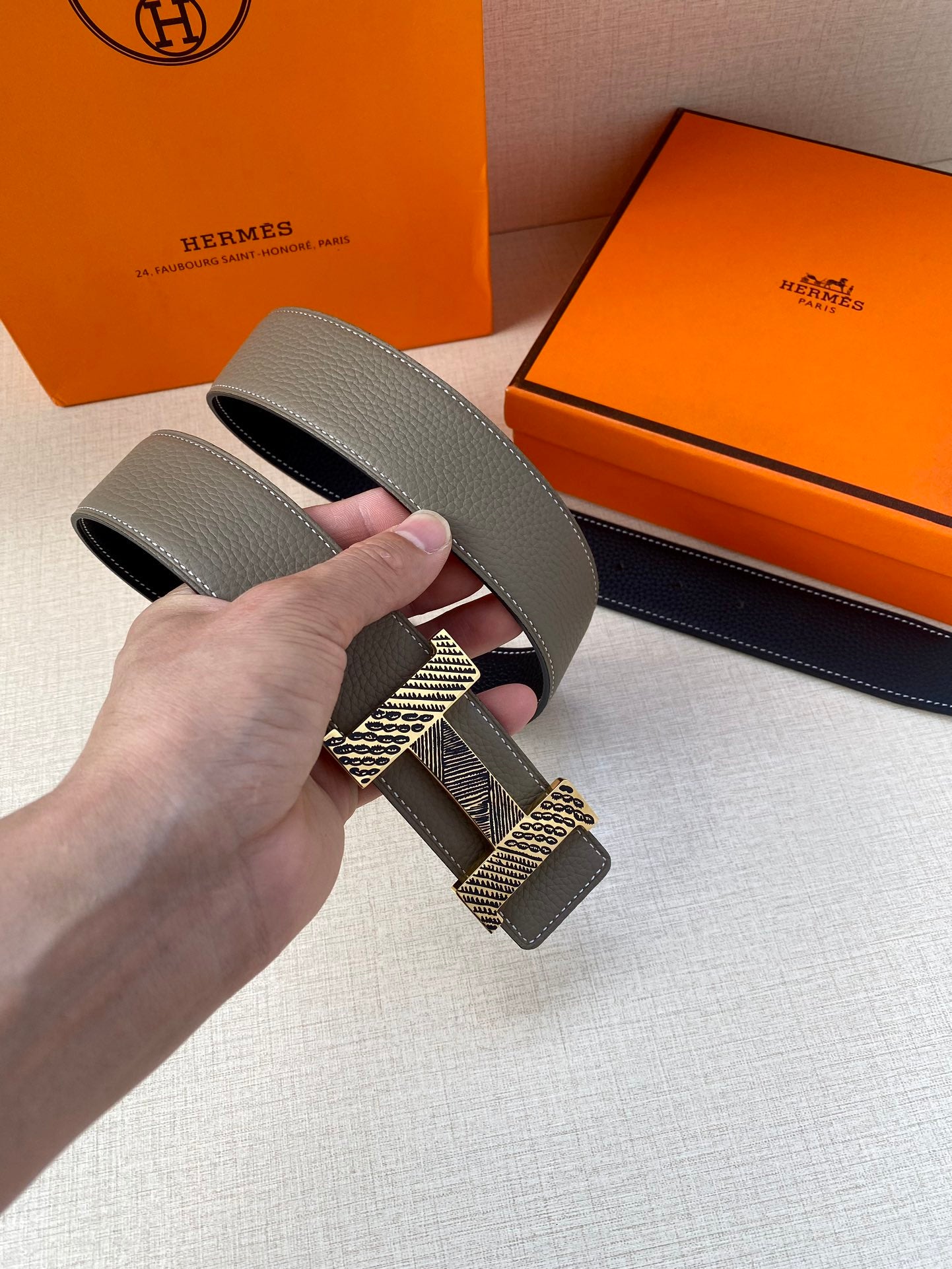Grey leather belt strap with textured gold-tone buckle, close-up held in hand.