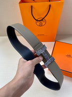 Grey leather belt held up, dark interior visible, textured gold-tone buckle and keeper.