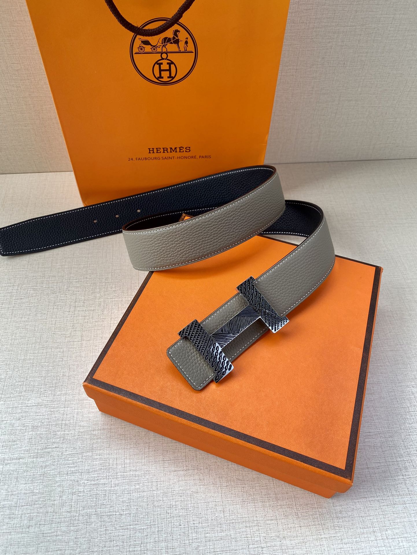 Grey leather belt with textured gold-tone buckle, side view with strap crossing.