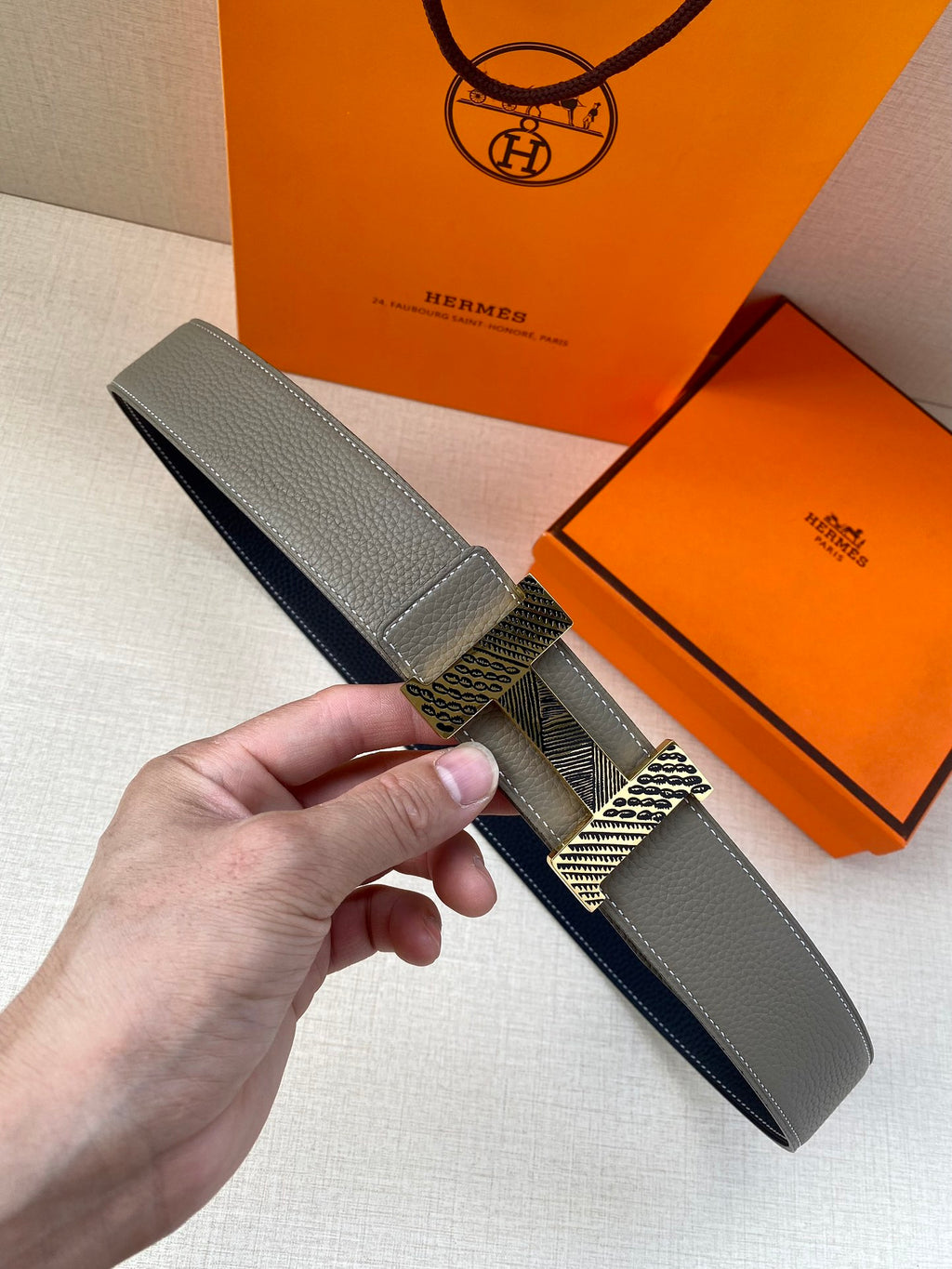 Grey leather belt with textured gold-tone buckle and keeper, folded end visible.