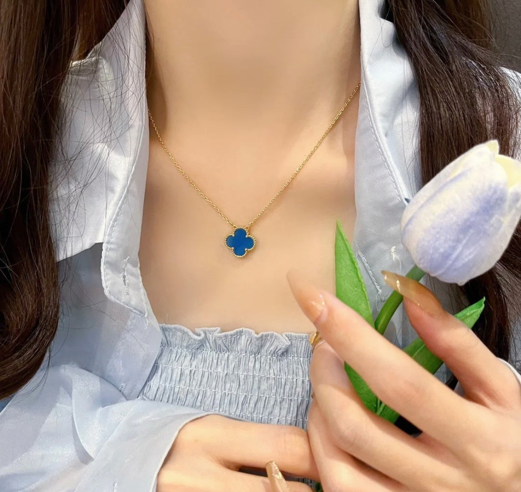Gold clover pendant necklace with blue enamel, worn at the neckline