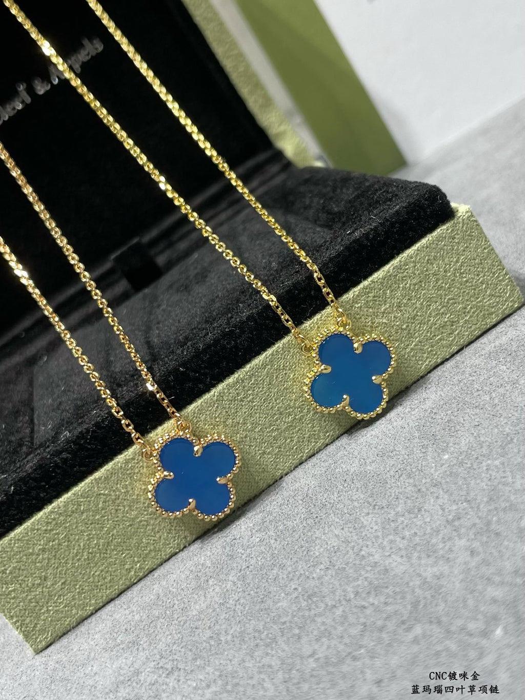 Gold clover pendant necklaces with blue enamel, lined up on a display tray