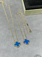 Gold clover pendant long necklaces with blue enamel, shown on a gray surface