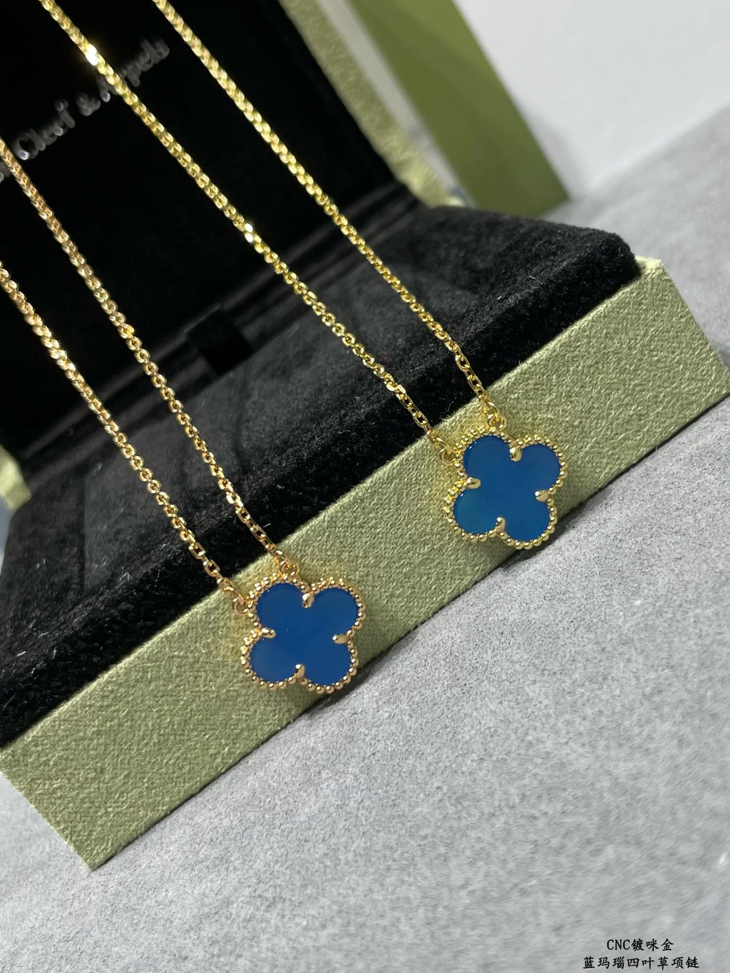 Gold clover pendant necklaces with blue enamel, shown on a black cushion display