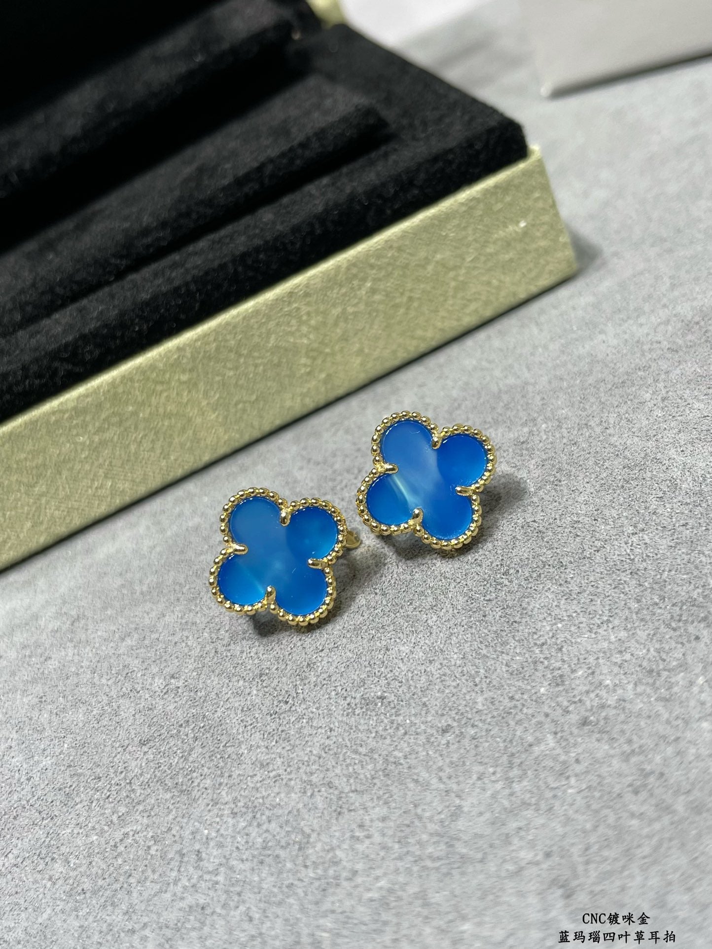 Two blue clover stud earrings with gold-tone frames on display