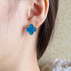Blue enamel quatrefoil stud earrings on model’s ear, gold-tone setting