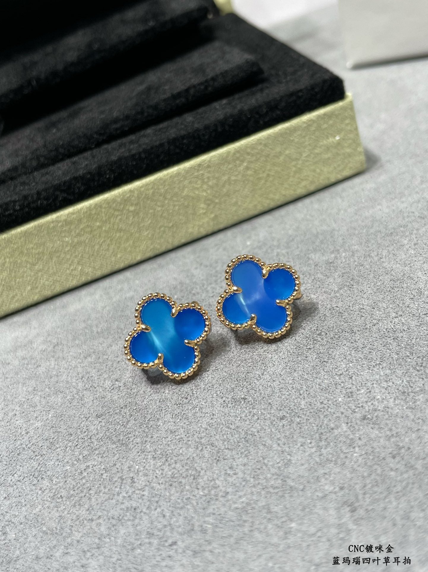 Pair of blue clover stud earrings with gold-tone frames on gray surface