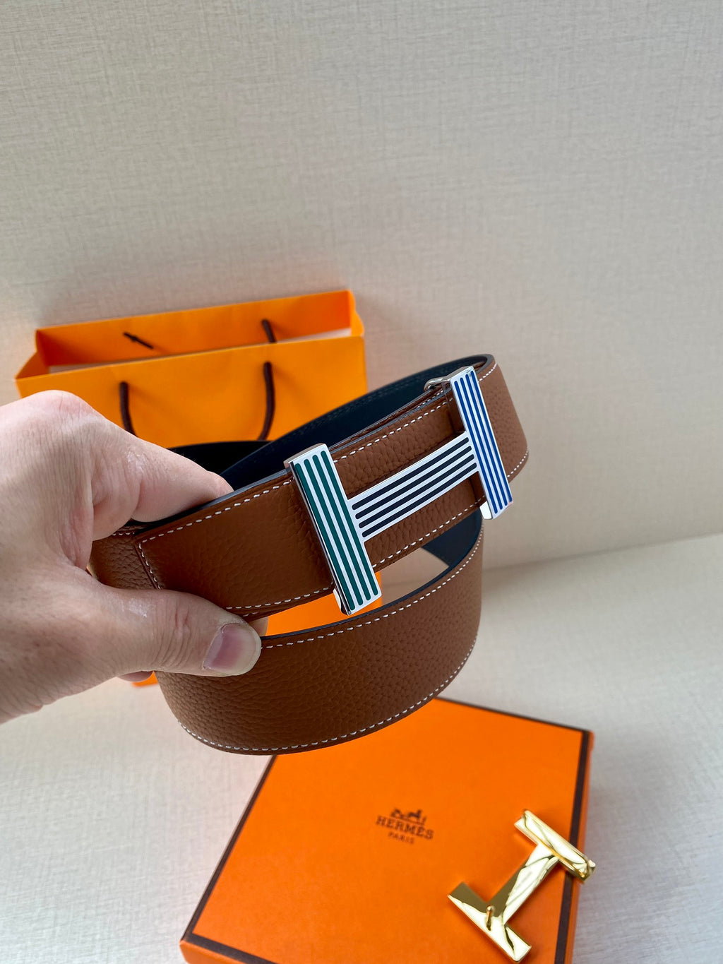 Brown leather belt close-up with striped green and blue buckle and orange packaging