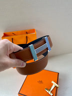 Brown leather belt close-up with striped green and blue buckle and orange packaging