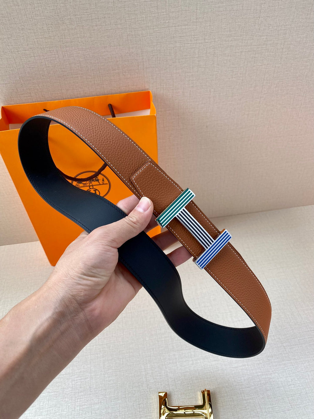 Brown leather belt with striped buckle and black underside strap shown
