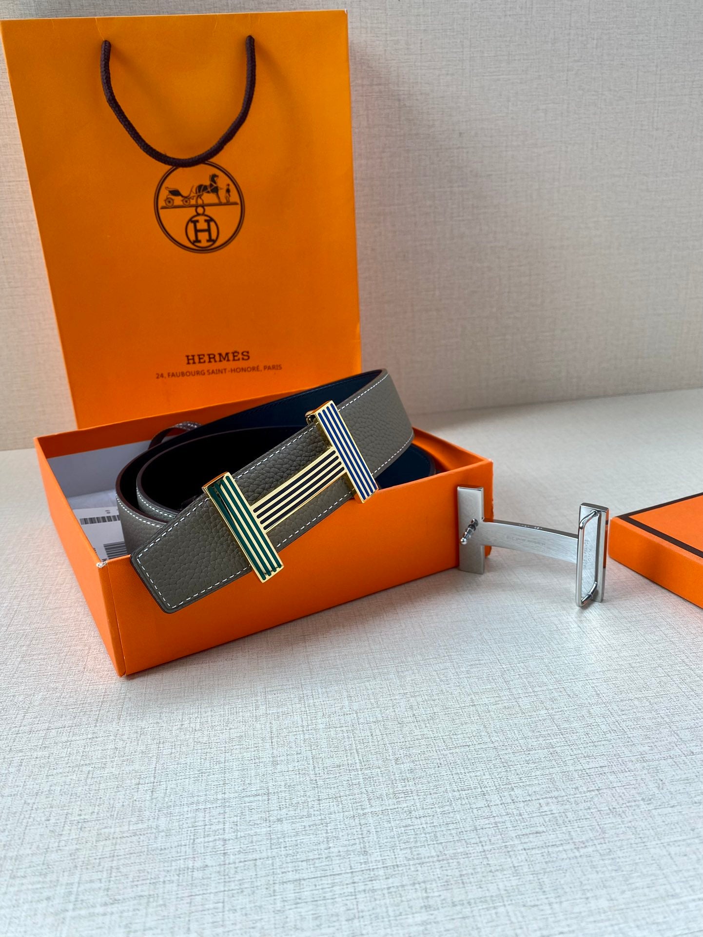 Hermes belt gray leather with striped buckle, shown in orange gift box with accessories