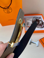 Hermes belt buckle close-up on gray leather strap with striped inlay and gold hardware