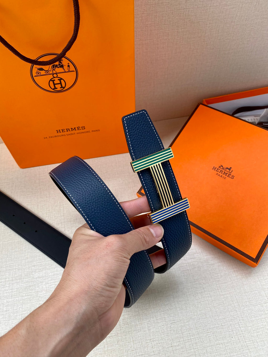 Blue leather belt with striped buckle and visible leather edge stitching.