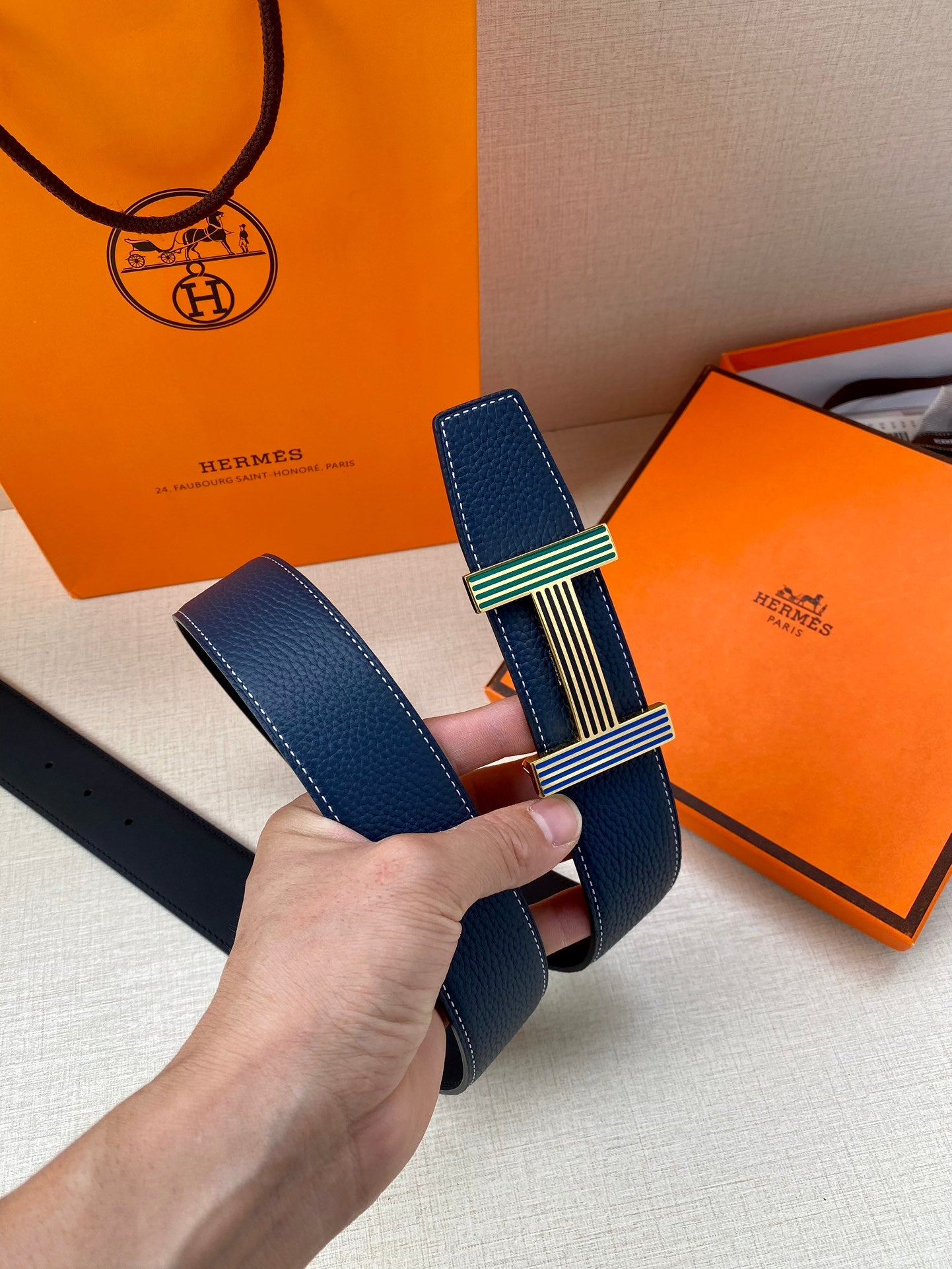 Blue leather belt with striped buckle and gold-tone clasp, held upright